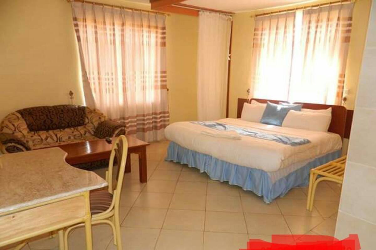 Quarto com cama, cadeira, mesinha e cortinas.