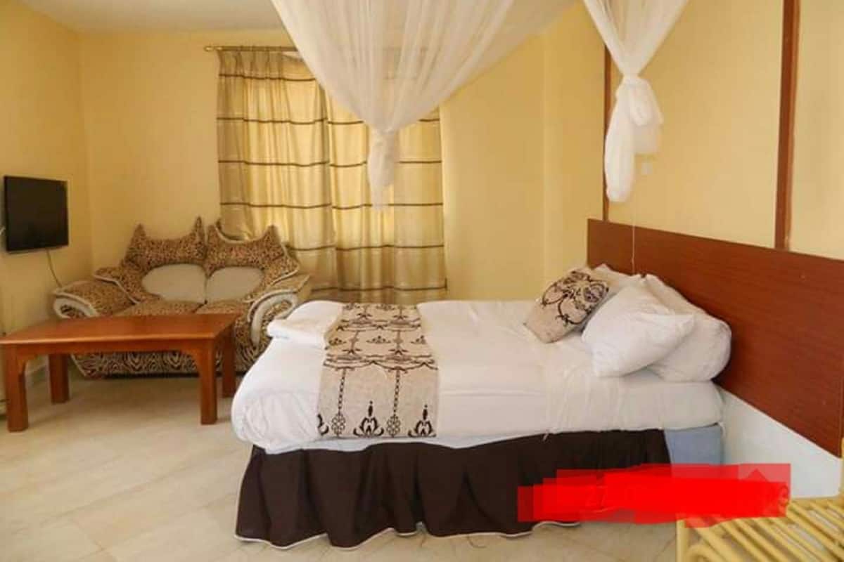 Quarto com cama, mesa de cabeceira, cadeira e televisão.