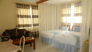 Habitación de hotel con dos camas, un sofá, una mesa y cortinas.