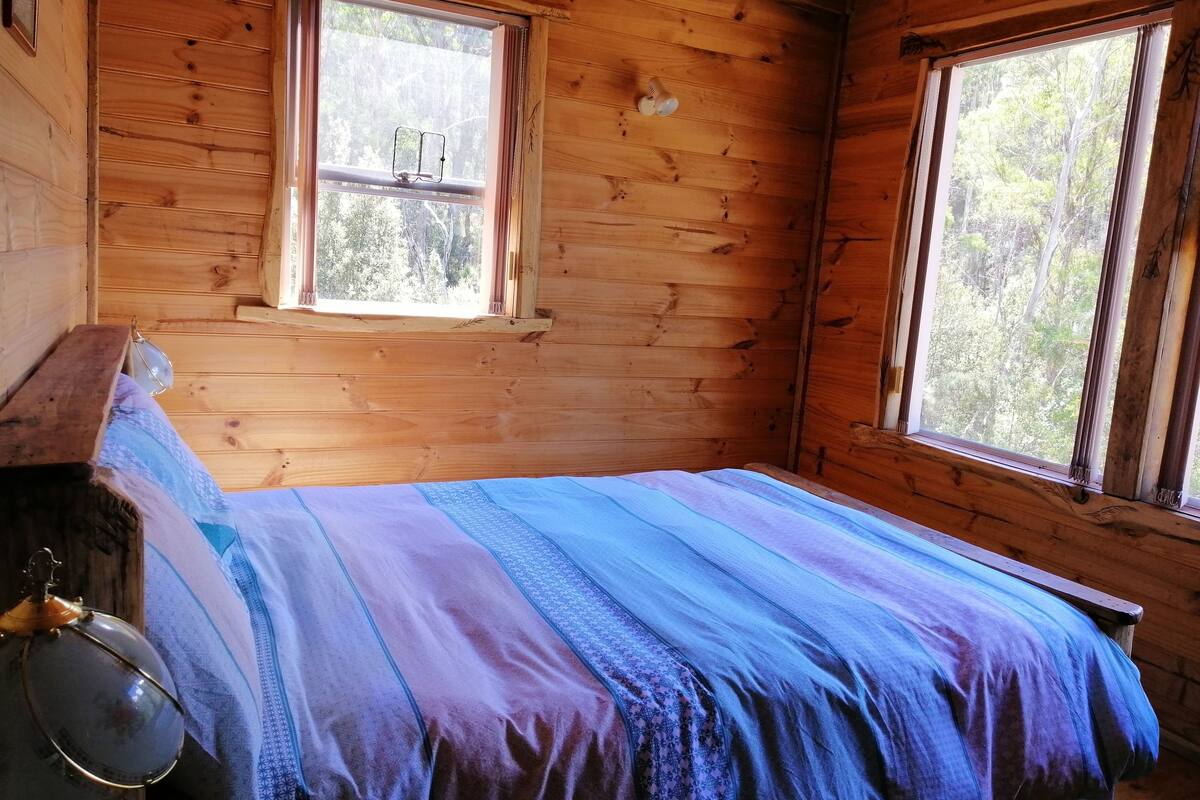 Una stanza in una baita di legno con un letto, una finestra e una lampada a sospensione.
