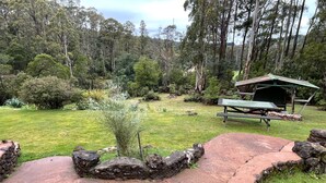 Un área de picnic con un banco de piedra y una mesa, rodeada por un campo de césped y árboles.