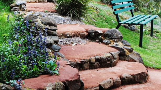 Un sendero de piedra que lleva a un banco en un jardín.