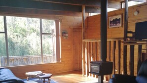 Interior acogedor de una cabaña con suelo de madera, un sofá, un sillón, una mesita y una chimenea.