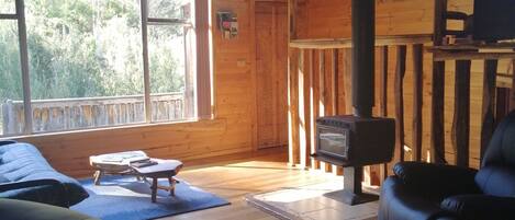 A cozy cabin interior with a wooden floor, a sofa, a chair, a small table, and a fireplace.
