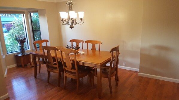 A dining room with a wooden table and chairs, a chandelier, and a window with a view of greenery.