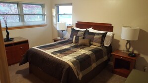 A neatly made bed with a quilt, two bedside lamps, a nightstand, and a window with blinds. - West Yakima - Clean - Safe - Netflix - 4212 - ONWU-LLC (Yakima)
