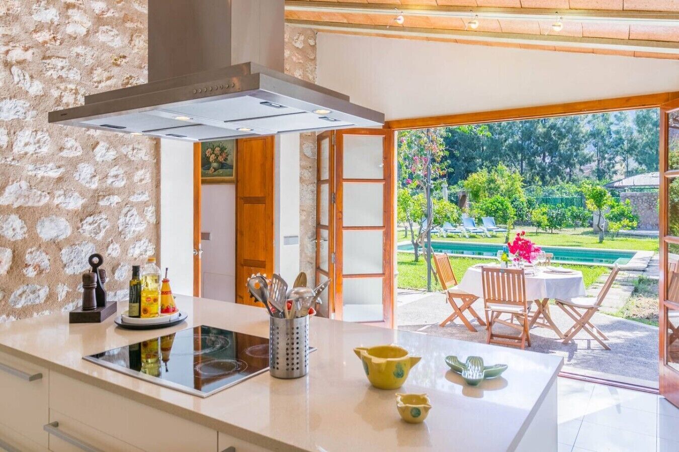 A modern kitchen with a large island, a dining area with outdoor seating, and a view of a pool and garden.