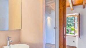 A bathroom with a white sink, a mirror, and a wooden door leading to a room with a window. - Captivating Mallorcan Villa With A Pool In Soller (Sóller)
