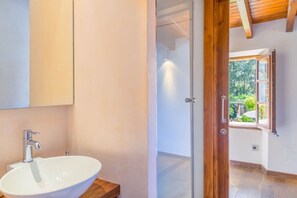 A bathroom with a white sink, a mirror, and a wooden door leading to a room with a window.