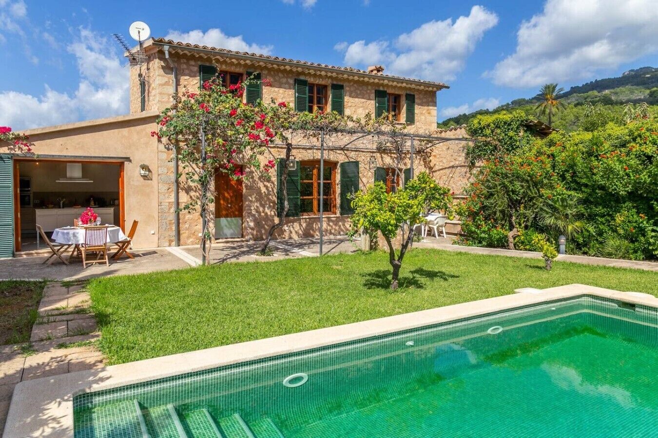 Un edificio de piedra de dos plantas con piscina, un patio amoblado y un jardín exuberante.