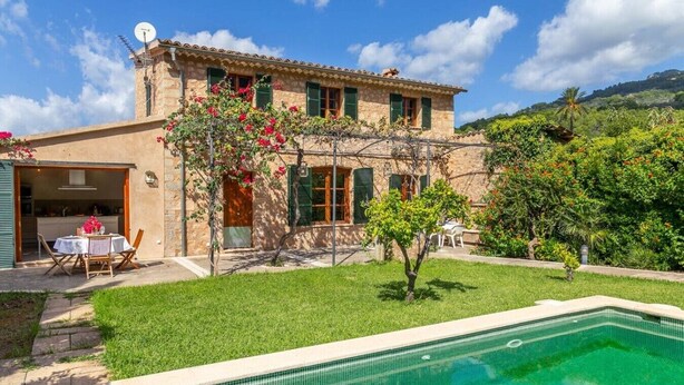A two-story stone building with a swimming pool, a patio with outdoor furniture, and a lush garden. - Captivating Mallorcan Villa With A Pool In Soller (Sóller)