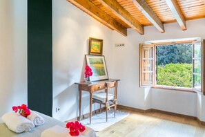 Une pièce avec un plafond en bois, un bureau sur lequel est posée une photo encadrée, une fenêtre avec un volet ouvert, et une vue sur la verdure à l’extérieur.