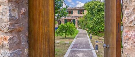 A pathway leading to a stone building with a tiled roof, surrounded by greenery and a clear sky.