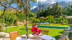 An outdoor dining area with a table set for two, surrounded by lush greenery and a mountain backdrop. - Captivating Mallorcan Villa With A Pool In Soller (Sóller)