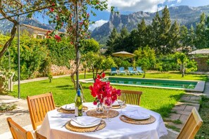 An outdoor dining area with a table set for two, surrounded by lush greenery and a mountain backdrop.