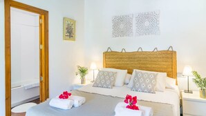 A hotel room with a wooden headboard, two bedside tables with lamps, a bed with patterned pillows, and a door leading to a shower area. - Captivating Mallorcan Villa With A Pool In Soller (Sóller)