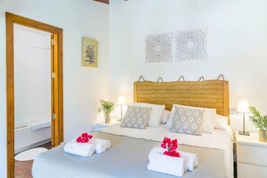A hotel room with a wooden headboard, two bedside tables with lamps, a bed with patterned pillows, and a door leading to a shower area.