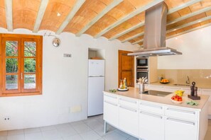 Une cuisine avec des armoires blanches, un four encastré, une hotte de cuisinière en acier inoxydable et une fenêtre donnant sur un paysage verdoyant.