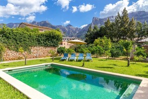 A swimming pool with lounge chairs, surrounded by greenery and mountains in the background.