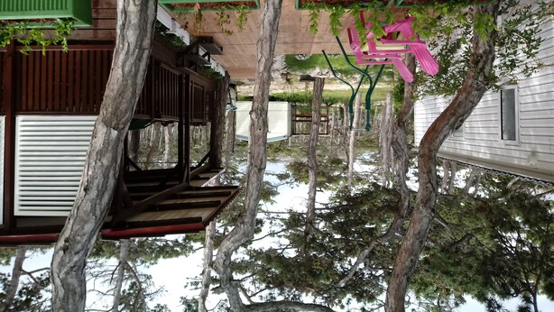 A rustic outdoor area with wooden structures and trees, featuring a swing set and a green roofed bench. - Kamp Planik- Campsite (Razanac)