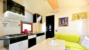 A compact kitchen with a stove, sink, and white cabinets. There's a green sofa with a cushion and a small table with a decorative item. - Kamp Planik- Campsite (Razanac)