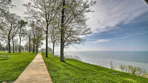 A park with a concrete path, green grass, trees, and a body of water in the background.