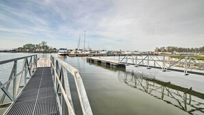 A marina with a wooden dock extending into calm water, surrounded by boats and a clear sky.
