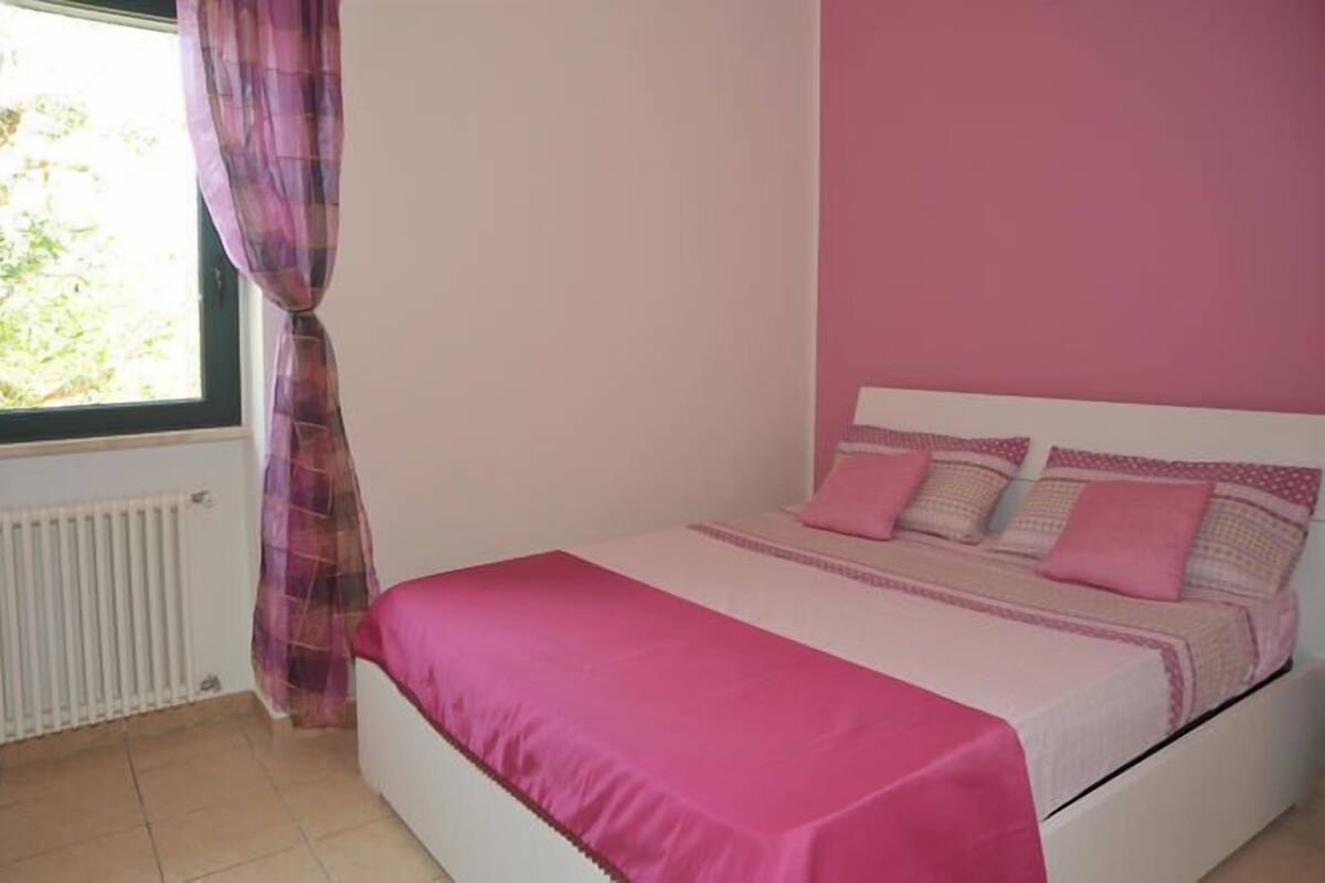 Un dormitorio con cama, ventana con cortinas y radiador.