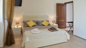 A bedroom with a bed, two bedside lamps, a TV mounted on the wall, and a door to another room. - Vacanze al Minci (Giurdignano)