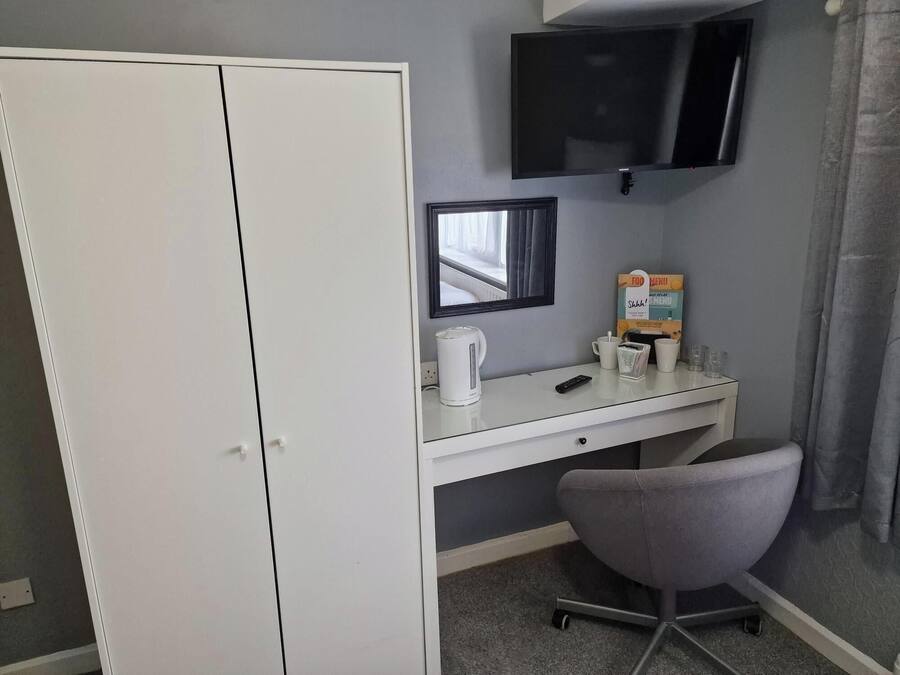 A hotel room with a white desk, a chair, a flat-screen TV, a framed picture, a kettle, and a breakfast menu.