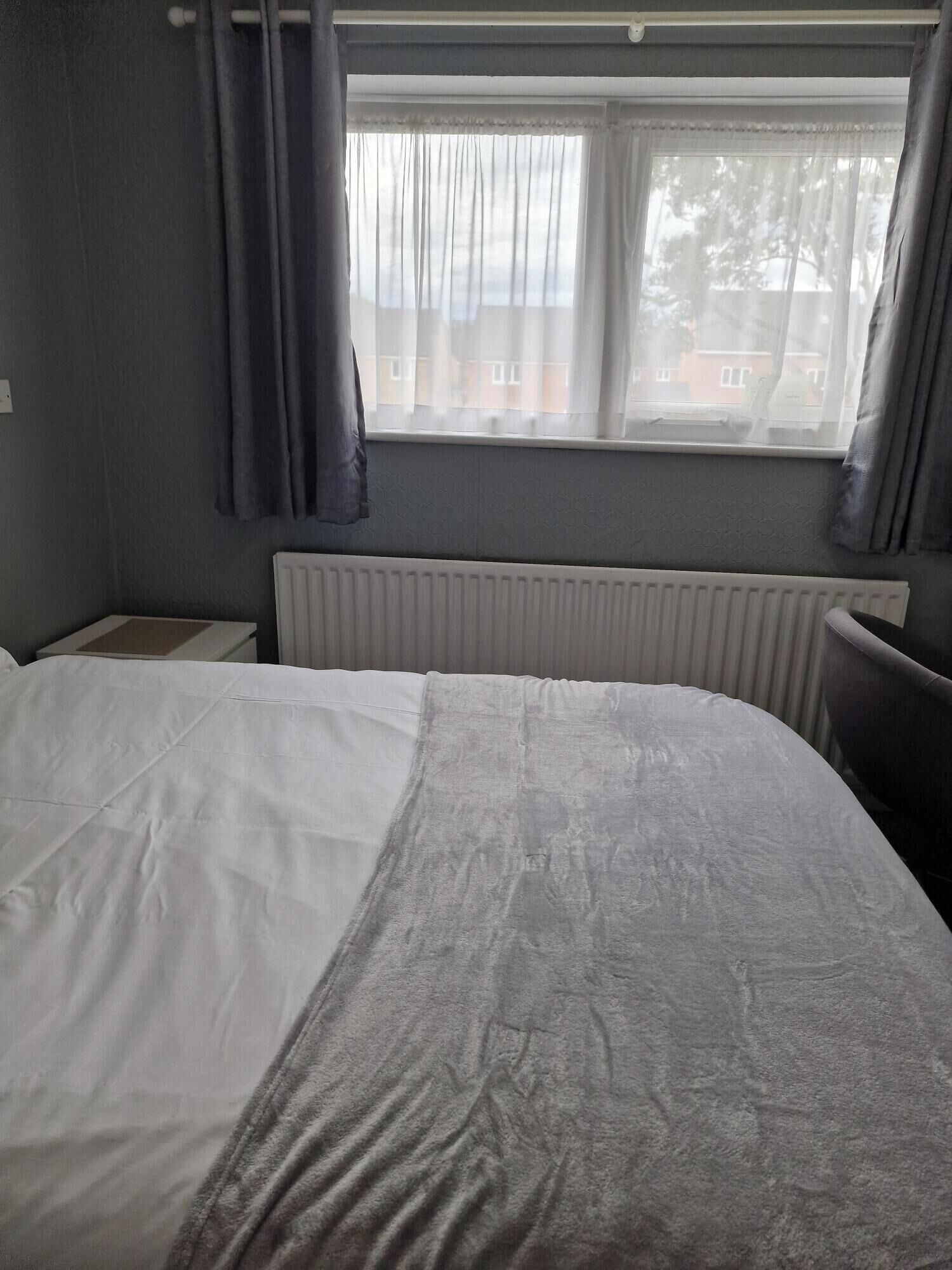 A hotel room with a bed, a radiator, and a window with curtains.
