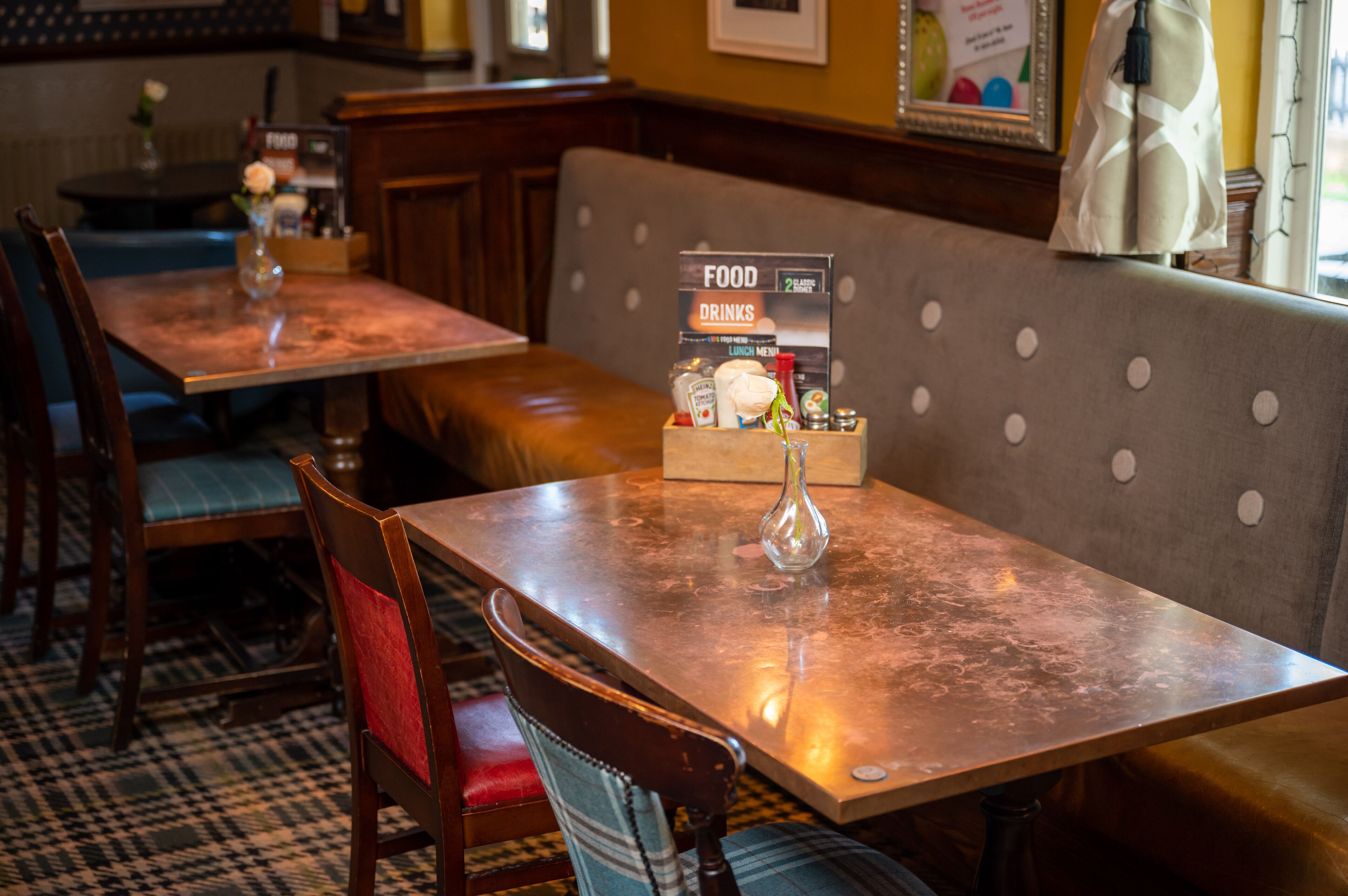 A restaurant interior with wooden tables and benches, a menu stand, and a patterned floor.