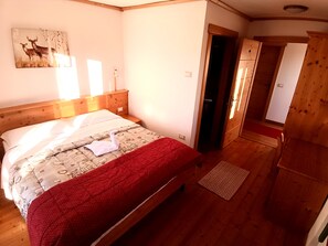 A wooden-framed bed with a patterned bedspread and a red blanket, a wall-mounted picture of deer, and a wooden wardrobe.