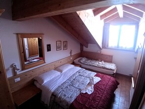 A bedroom with two beds, wooden beams, a window, and a mirror.