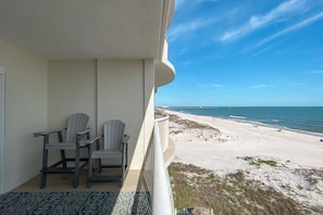 Enjoy stunning views of the beach from this balcony, featuring two comfortable chairs and a small table.