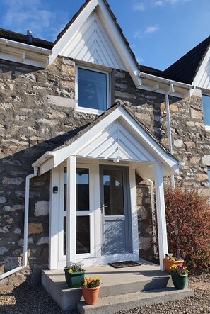 A stone house with a white front porch and a small window.