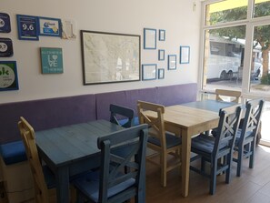 A dining area with wooden tables and blue chairs, a purple cushioned bench, and framed pictures on the wall. - Camping Odmoree - Campsite (Razanac)