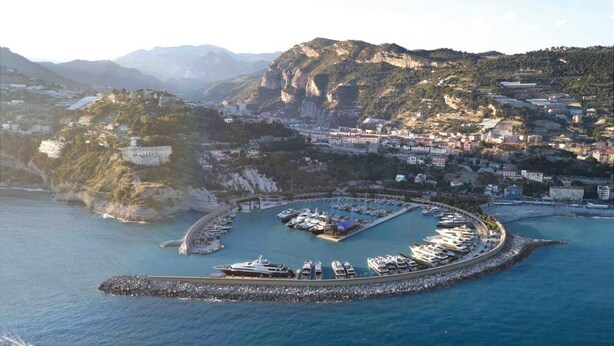 Vista aérea de un pueblo costero con un puerto deportivo, edificios y un acantilado imponente.