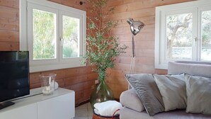 Una habitación con paneles de madera, un televisor sobre un mueble blanco, un sofá gris, un jarrón con plantas y una lámpara de pie.