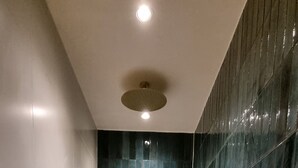 Una ducha moderna con suelo de mármol, cabezal de ducha dorado y paredes revestidas de azulejos azul oscuro.