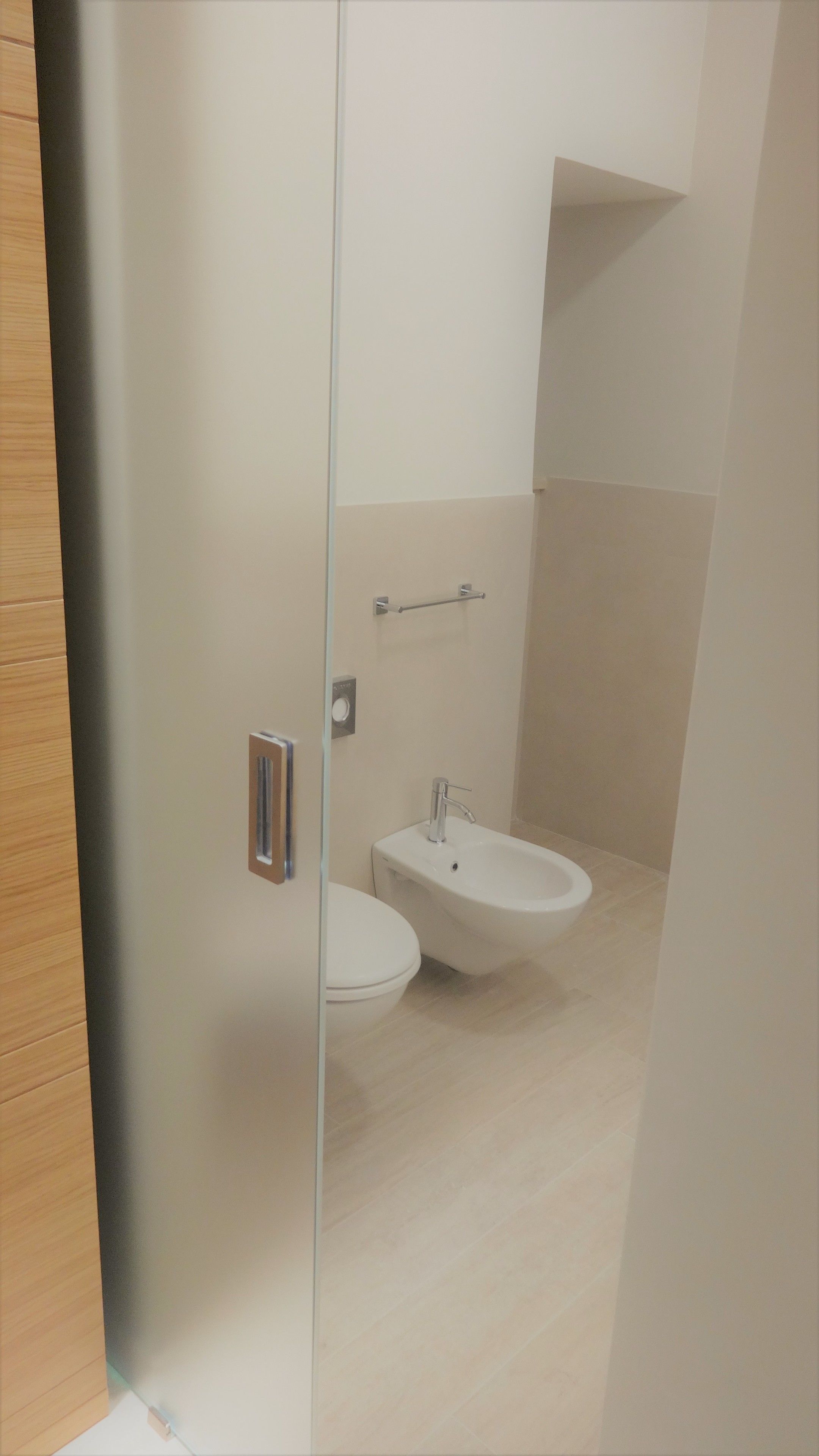 A modern bathroom with a toilet, bidet, and a towel rack.