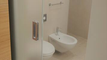 A modern bathroom with a toilet, bidet, and a towel rack.
