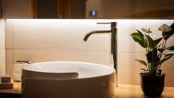 A modern bathroom with a white vessel sink, a chrome faucet, and a potted plant on the counter.