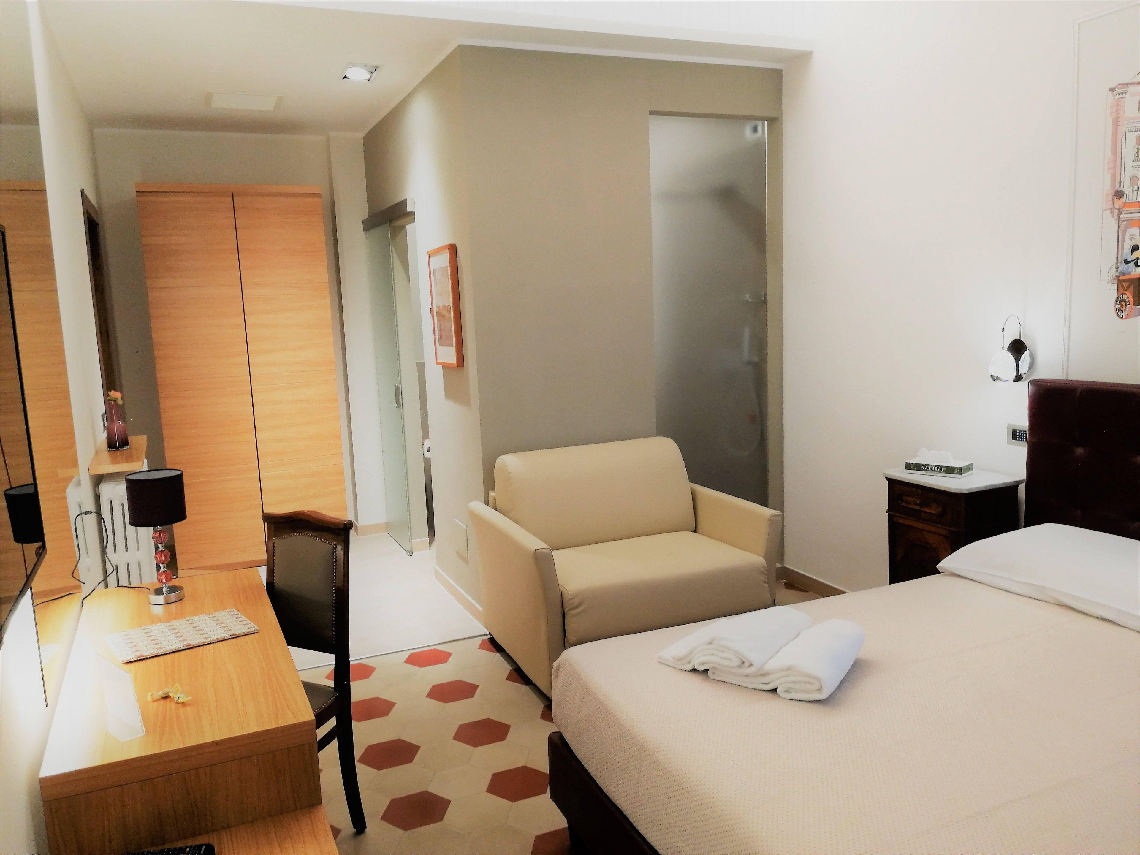 Une chambre d’hôtel comprenant un lit, un bureau, une chaise, une armoire et un espace douche.