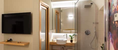 A modern bathroom with a TV mounted on the wall, a sink with a mirror, and a shower area.