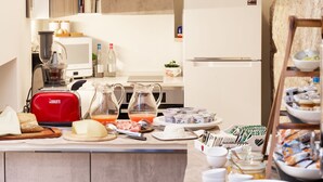 Una encimera de cocina con una tostadora roja, una licuadora, una jarra de jugo de naranja y diversos alimentos para el desayuno.