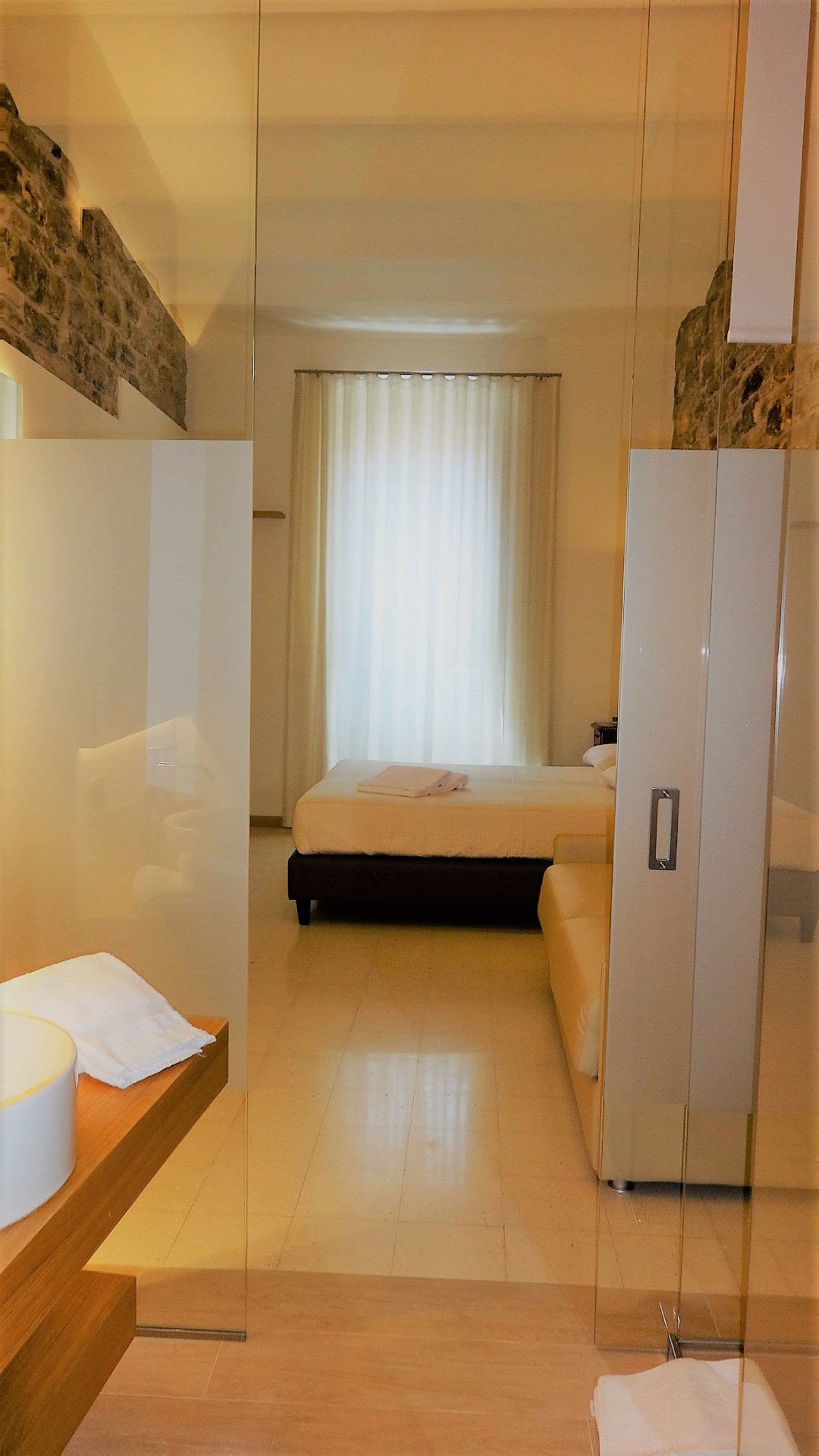 A modern hotel room with a bed, a wooden side table, a mirror, and a wardrobe.
