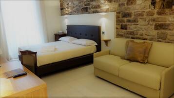 Una habitación de hotel con cama, sofá, escritorio de madera y pared de piedra.