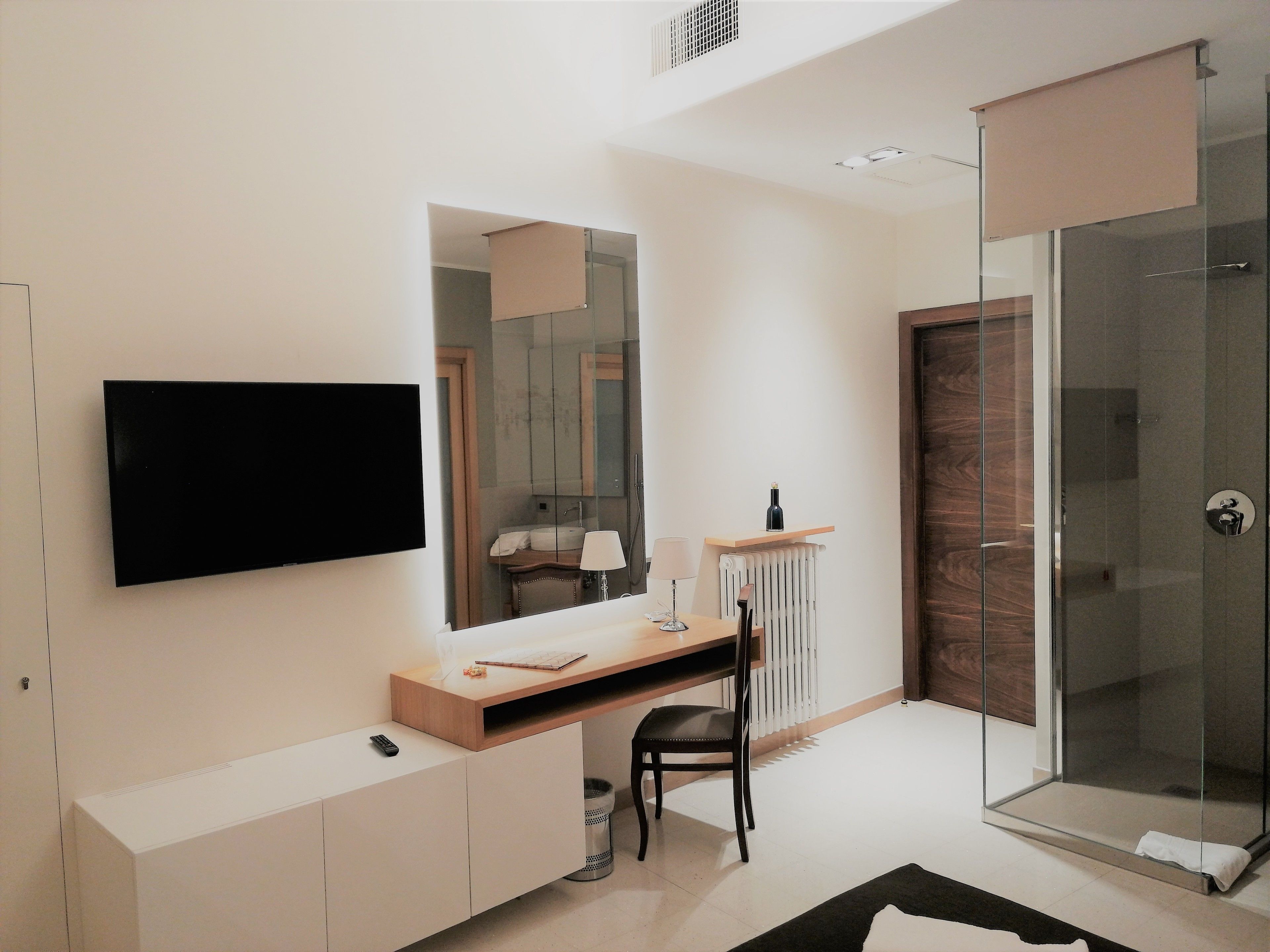 Une salle de bain moderne dotée d’une douche à parois de verre, d’un téléviseur fixé au mur et d’un meuble-lavabo avec un miroir.