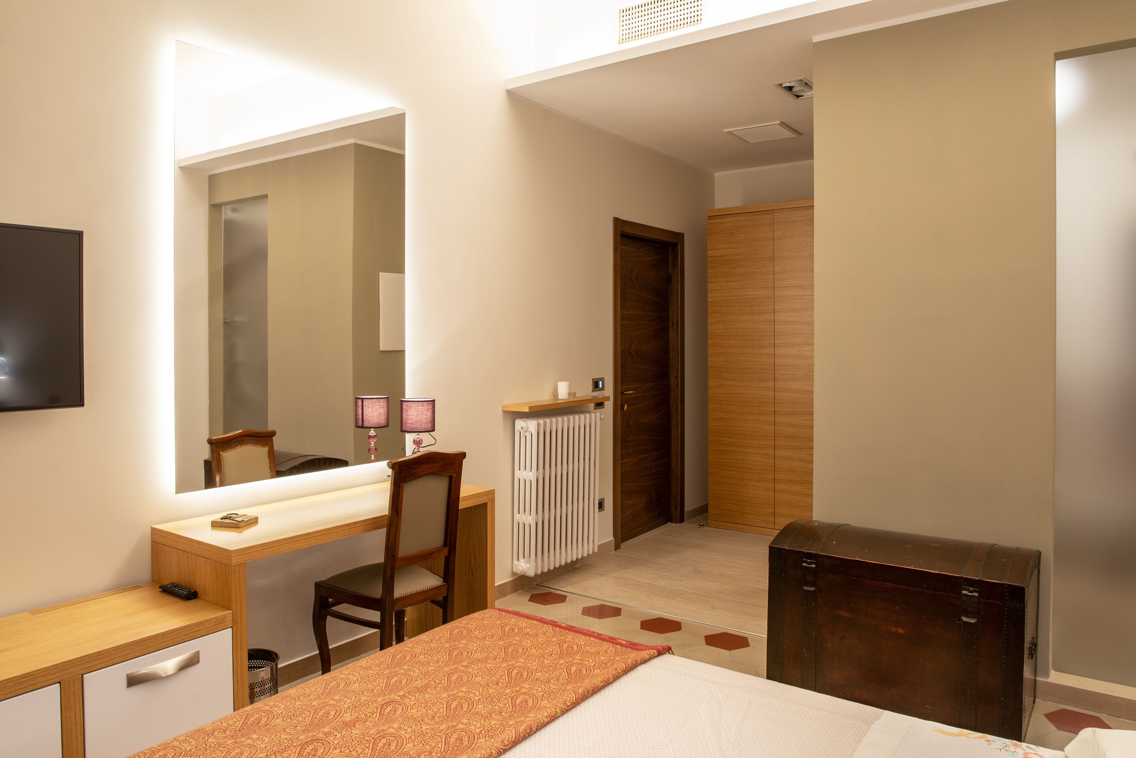 Hotelkamer met een bed, een bureau met stoel, een dressoir, een spiegel, een radiator en een kledingkast.